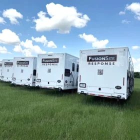 A row of white FusionSite Response trailers is parked in an open grassy field under a bright blue sky with scattered clouds.