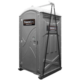 A gray portable restroom with a FusionSite logo attached to lifting straps and a metal frame, prepared for crane transport at a construction site.