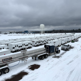 Fleet of FusionSite Response portable restroom trailers and water tanker trucks staged in a snow-covered lot with a water tower in the background
